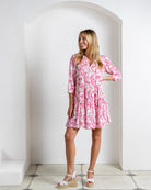 Model wearing silk crepe tiered Amy dress in Parrot pink print – luxury resortwear with 3/4 sleeves and buttoned V-neckline