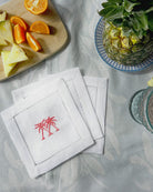 Embroidered linen cocktail napkins in Palms coral pink styled with fruit on a tropical table setting