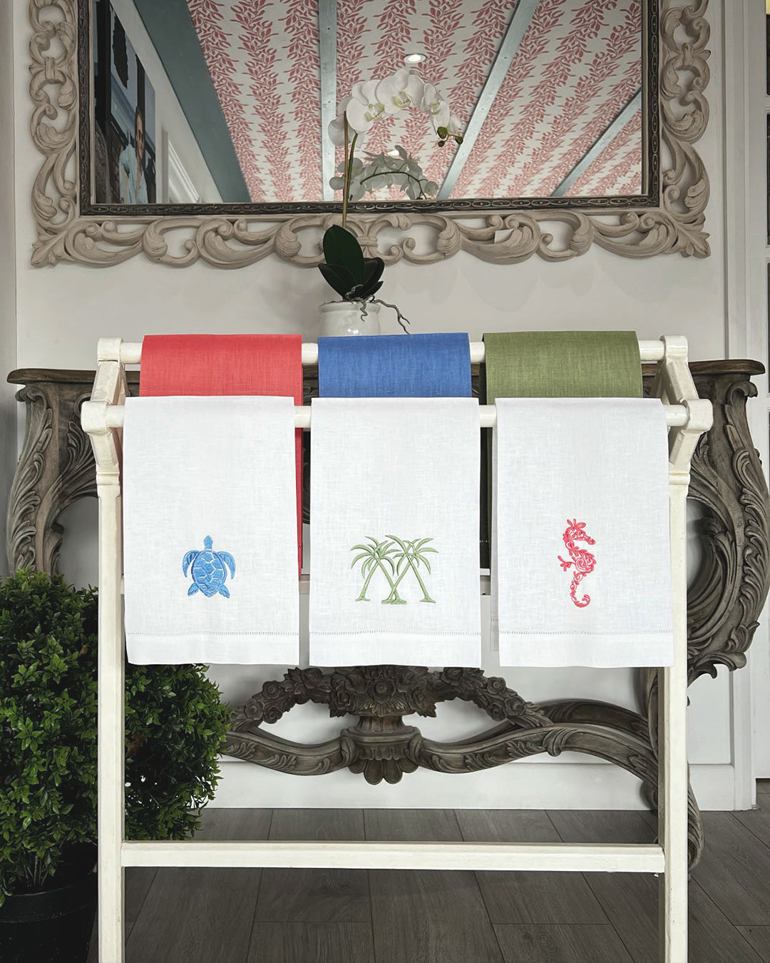 Luxury embroidered linen hand towels with palm, seahorse and turtle motifs displayed in the Pink House Mustique Semley showroom.