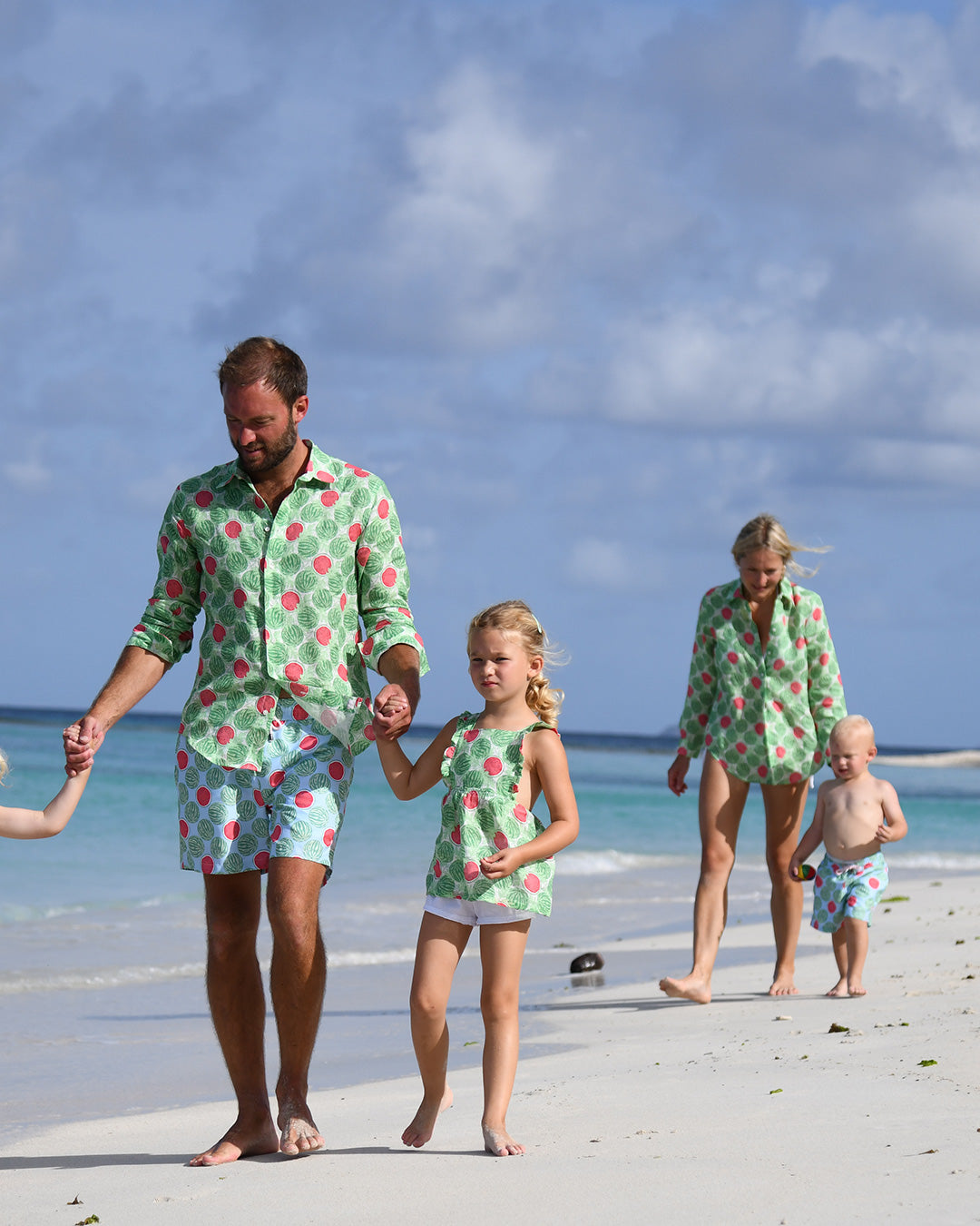 Family wearing matching Watermelon print resortwear and swim shorts on a Caribbean beach