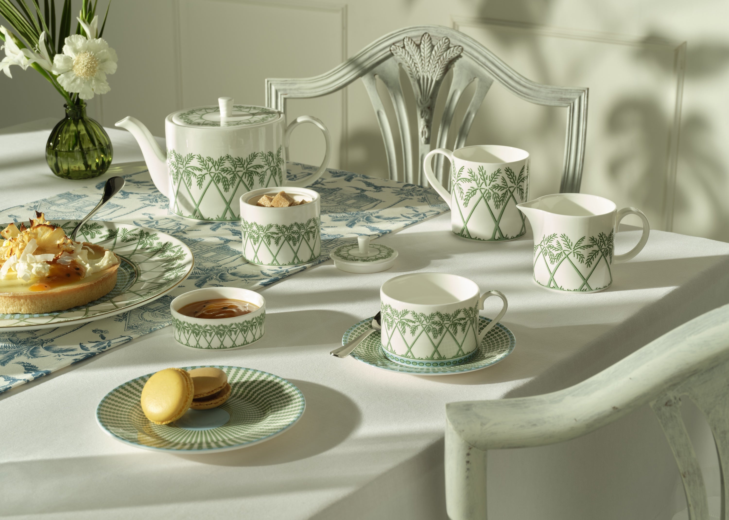 Tea set with green patterns on a table with pastries and a vase of flowers.