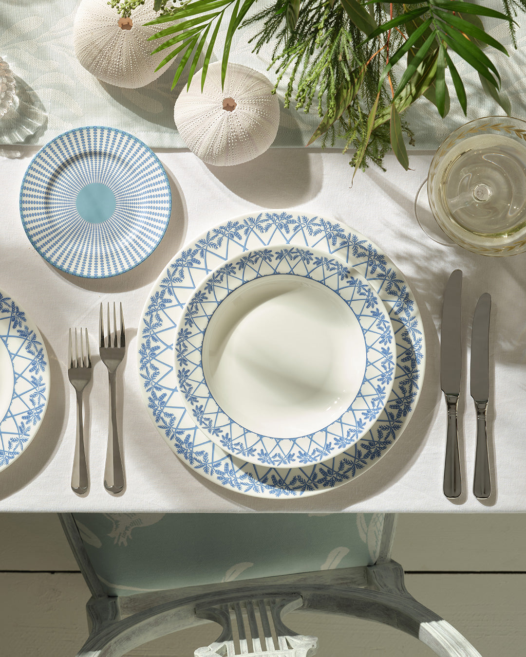 Dining table setting with blue and white Palms patterned rimmed bowl on a dinner plate.