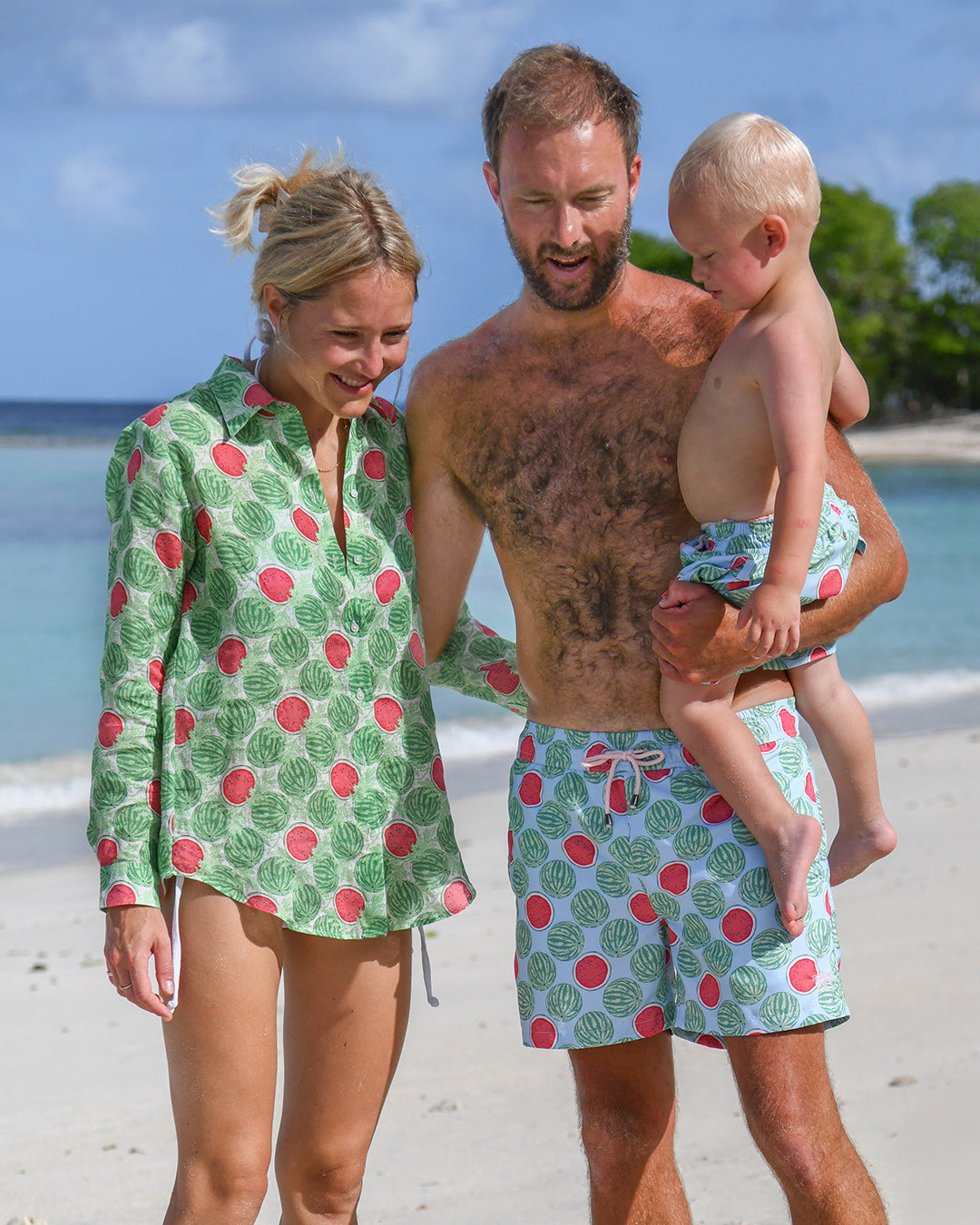 Family wearing matching Watermelon print resortwear and swim shorts on a Caribbean beach