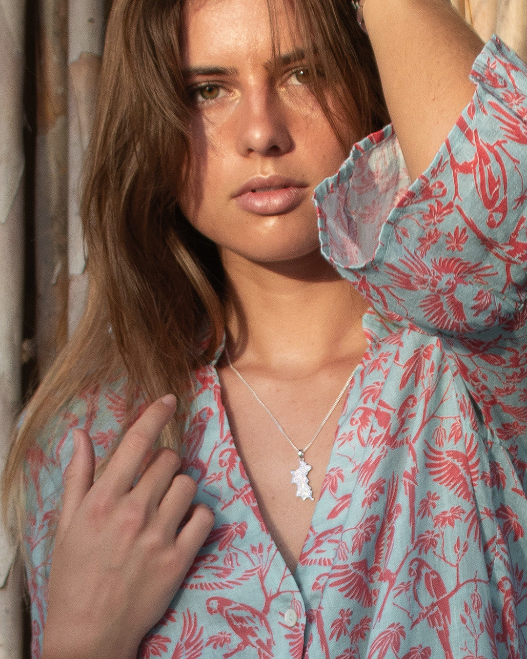 Close-up of Pink House Linen Decima Dress in Parrot Coral/Turquoise with Mustique Island silver pendant – features tropical bird pattern and gathered sleeve detail.