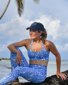 Madeline wearing navy blue Pink House Mustique cap with Parrot Blue activewear set, photographed on Lagoon Beach Mustique.