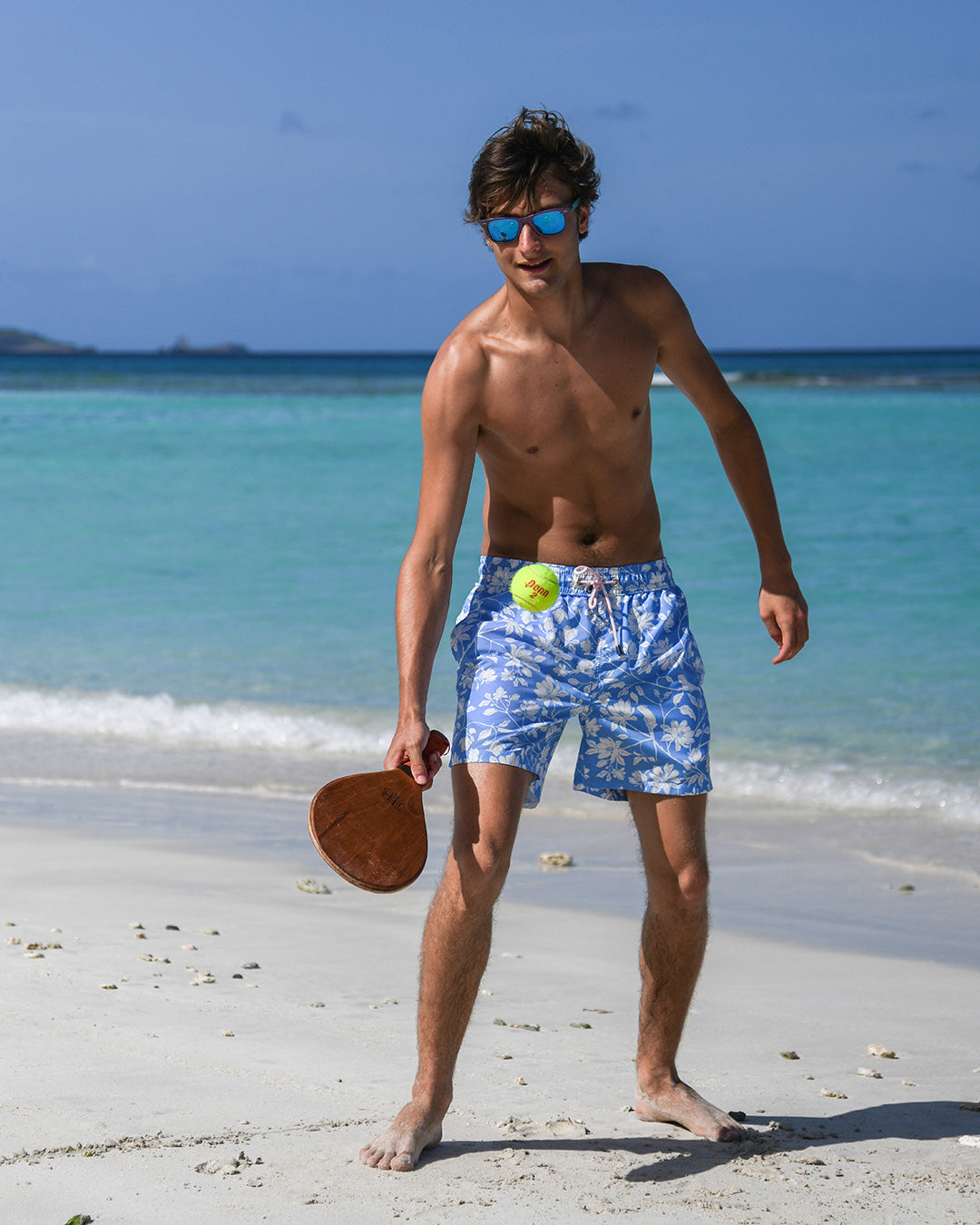 Fast-drying Iguana Blue men’s swim shorts with elasticated waist and mid-thigh fit, playing paddle ball on Mustique.