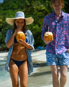 Couple wearing Iguana Blue & Pink linen shirt and Parrot Blue silk shirt with sarong and hat, walking at Brittania Bay, Mustique beach.
