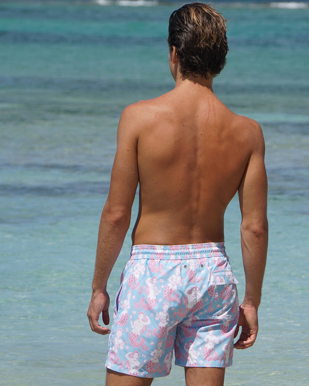 Back view of Pink House Mustique Mermaid Pink Blue swim shorts worn on the beach at Lagoon Bay Mustique