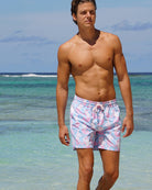 Man wearing Pink House Mustique Mermaid Pink Blue swim shorts walking in the sea at Lagoon Bay Mustique