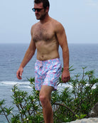 Man wearing Mermaid Pink Blue swim shorts walking beside the sea in Mustique
