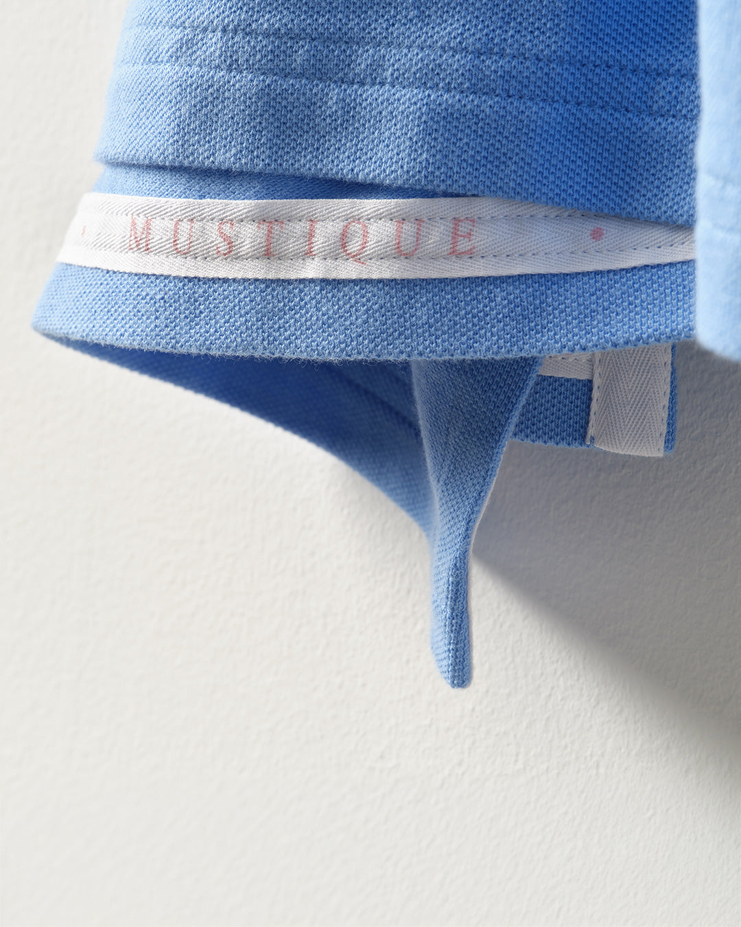 Close-up of the Pink House Mustique men's mid blue cotton polo shirt with signature Mustique neck tape detail