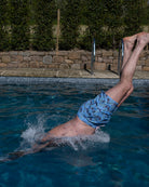 Man diving into a swimming pool wearing Pink House Mustique Monkey & Palms Plum swim shorts