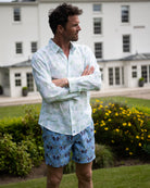Man wearing Monkey & Palms Plum swim shorts with a Green Palm linen shirt in a luxury garden setting