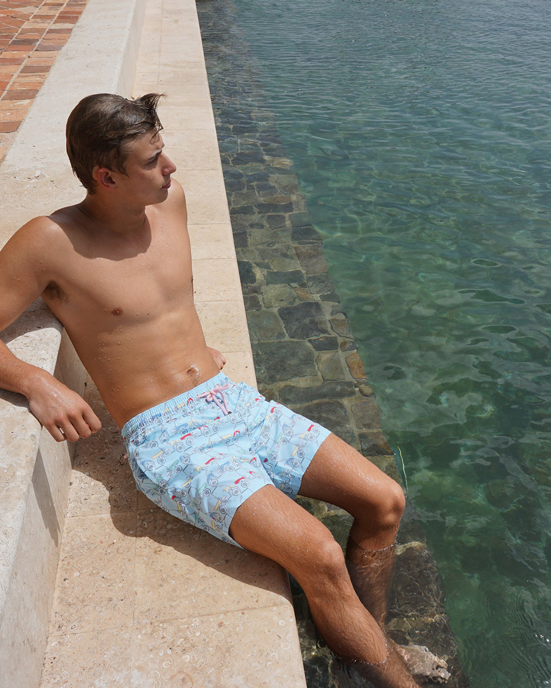 Man wearing Mustique Mule Multi swim shorts sitting poolside on Mustique
