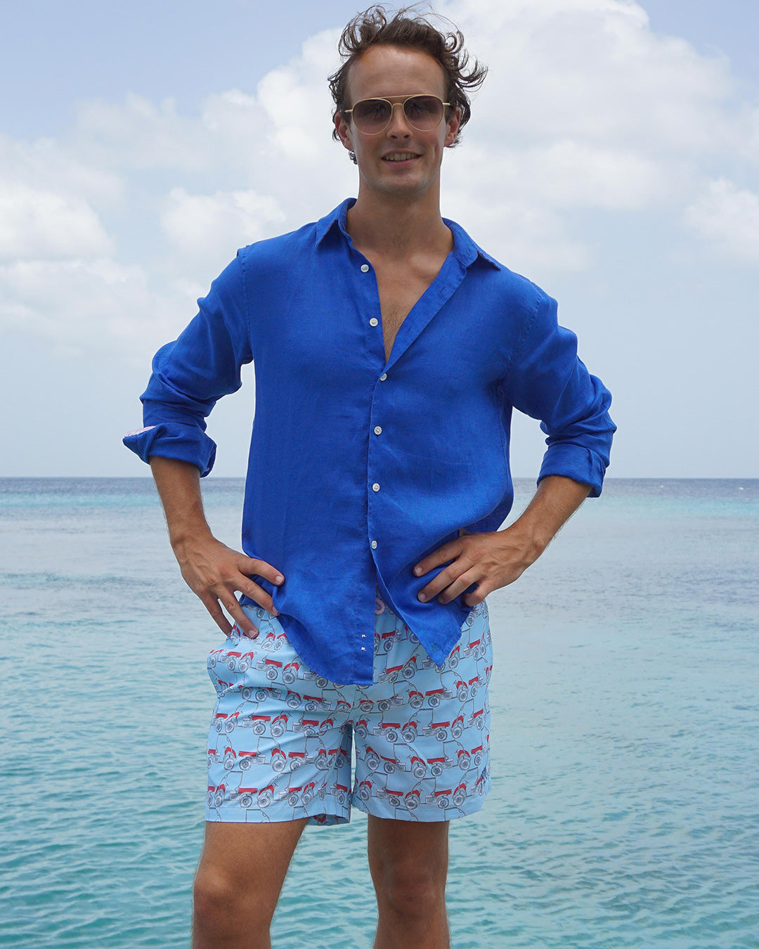 Men’s Mustique Mule red swim shorts styled with a blue linen shirt by the sea in Mustique