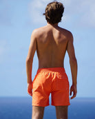 Men’s orange swim shorts back view by ocean, classic beach style and tailored fit