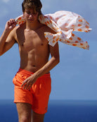 Men’s orange swim shorts on beach, shirt over shoulder, relaxed summer holiday style