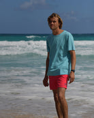 Men's pale blue cotton T-shirt styled with faded red swim shorts on the beach in Mustique