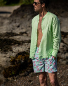 Mens pistachio green linen collarless shirt worn open on beach with monkey print swim shorts, grandad Nehru style