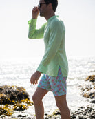 Mens pistachio green linen collarless shirt side profile on beach, grandad Nehru style with patterned swim shorts
