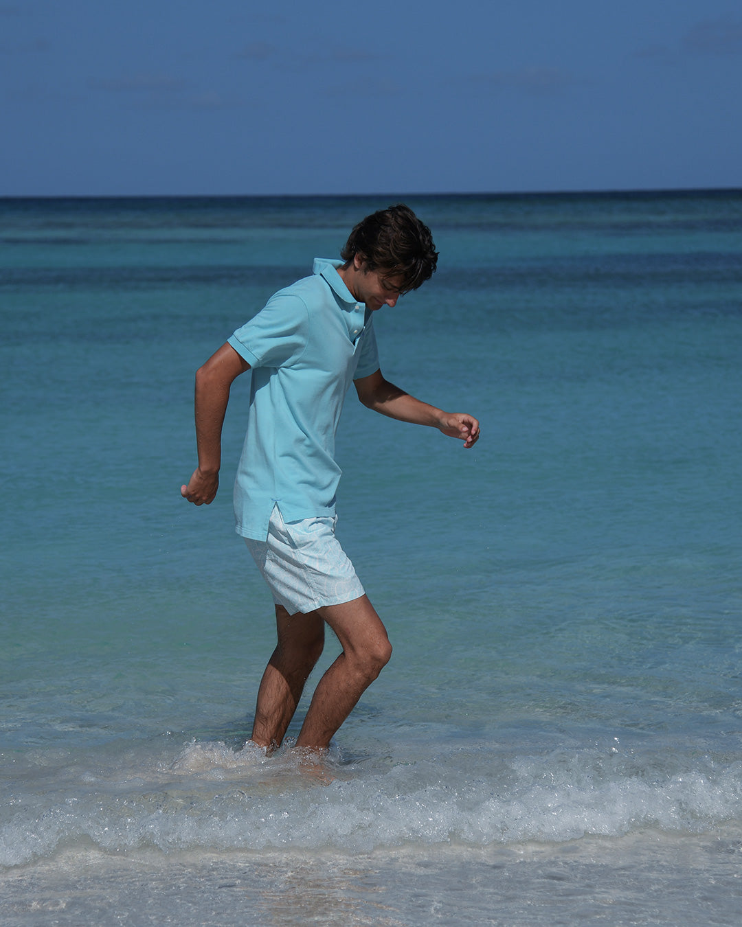 Men’s Coral Stone Aqua swim shorts by Pink House Mustique, walking by the lagoon in relaxed resort style.