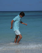 Men’s Coral Stone Aqua swim shorts by Pink House Mustique, walking by the lagoon in relaxed resort style.