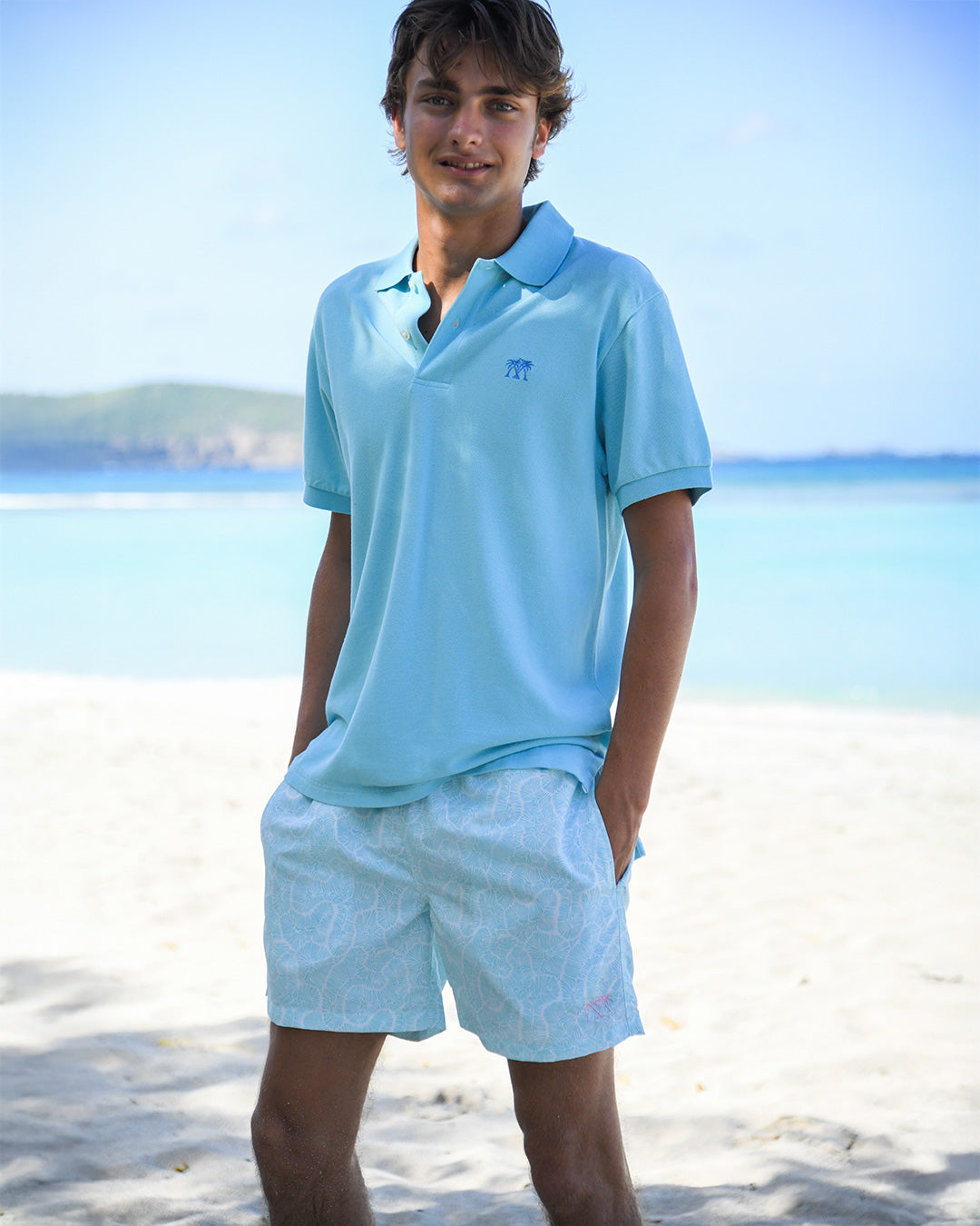 Men’s Coral Stone Aqua swim shorts styled with pale blue polo shirt by Pink House Mustique, luxury resortwear.