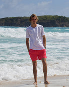 Men's white cotton T-shirt and faded red swim shorts by the sea on Mustique