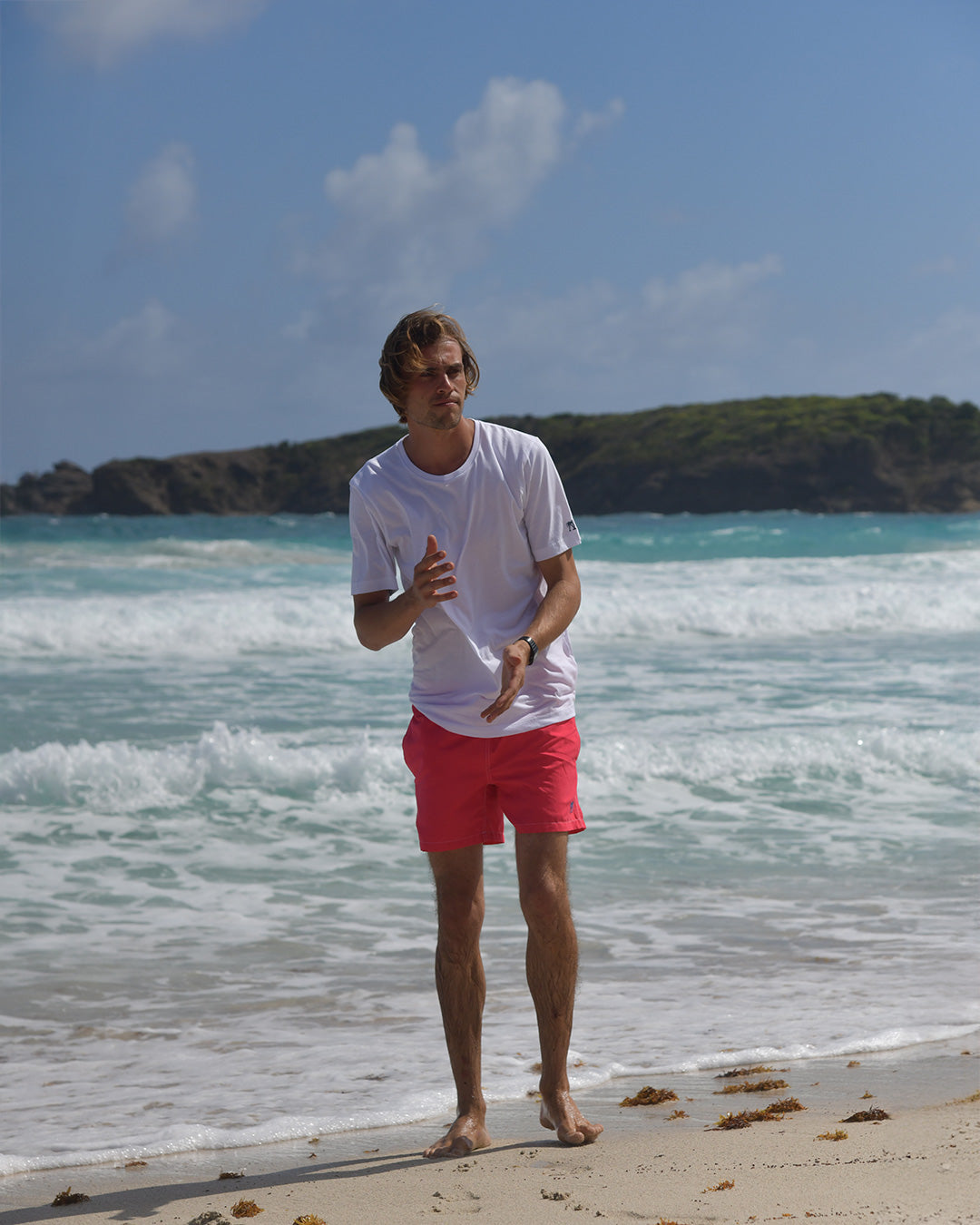 Men's white cotton T-shirt styled with faded red swim shorts on Mustique beach