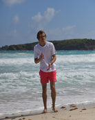 Men's white cotton T-shirt styled with faded red swim shorts on Mustique beach