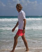 Men's white cotton T-shirt and faded red swim shorts walking along the shoreline in Mustique