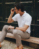 Close-up of a men's white cotton polo shirt with embroidered palm logo in a Mediterranean lifestyle setting.