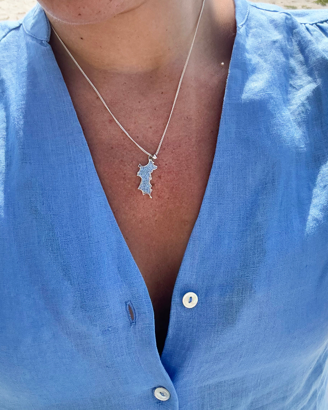 Mini Mustique island pendant necklace in sterling silver with blue zirconia crystals worn with blue linen dress Made in England