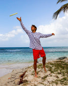 Fabian wearing Pink House Mustique collarless linen shirt in Gecko Navy print paired with red swim shorts – lightweight breathable resortwear ideal for beach holidays and tropical climates.