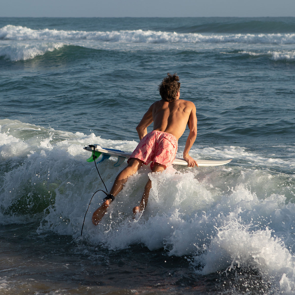 Men's ocean swim shorts in Fruit Punch Pink Orange worn while surfing in breaking ocean waves