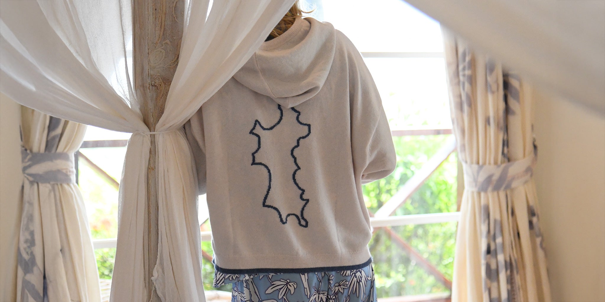 Back view of Malin Darlin x Pink House designer cashmere hoodie with Mustique island motif, styled with silk Parrot Blue silk pyjamas – coming soon