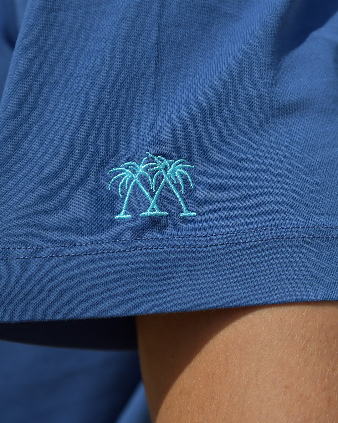 Close-up of Pink House Mustique embroidered crossed palms logo on navy men's cotton T-shirt sleeve