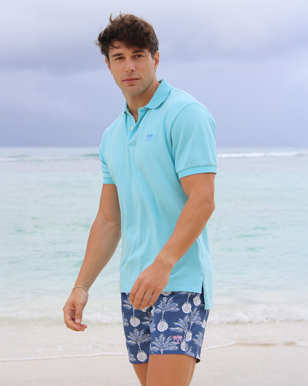 Pink House Mustique pale blue cotton polo shirt paired with Potted Palm navy swim shorts by the sea in Mustique