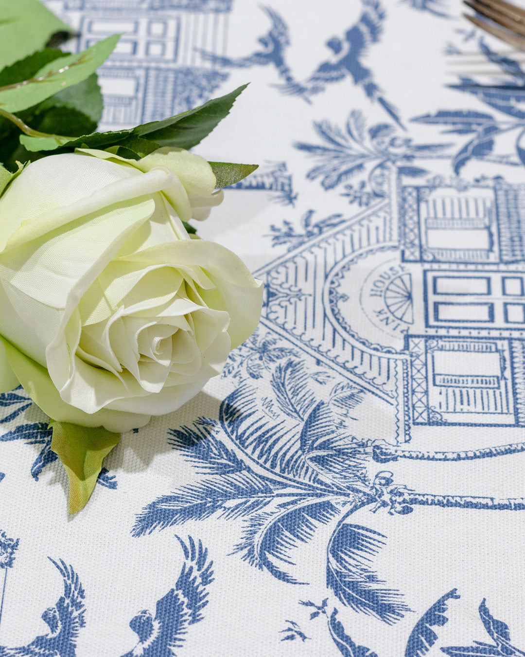 Detail of Pink House Toile blue cotton fabric featuring Pink House, palm trees, tropical birds and island foliage