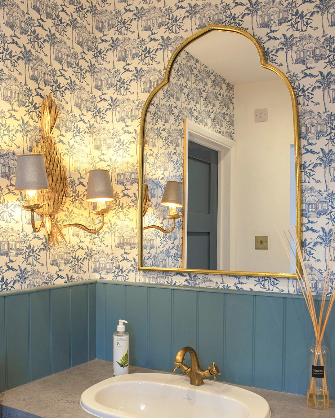 Pink House Toile Wallpaper in Semley Blue in a washroom with blue panelling, brass fittings and gold mirror