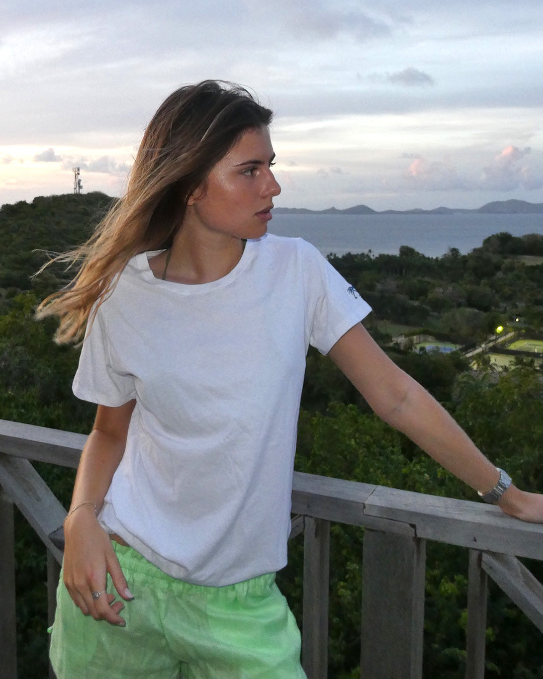 Woman wearing Pink House white pure cotton T-shirt overlooking the sea, classic Mustique beach essentials