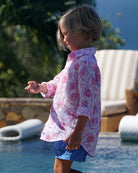 Child in unisex Pomegranate pink linen shirt and blue swim shorts walking poolside at Caribbean luxury villa