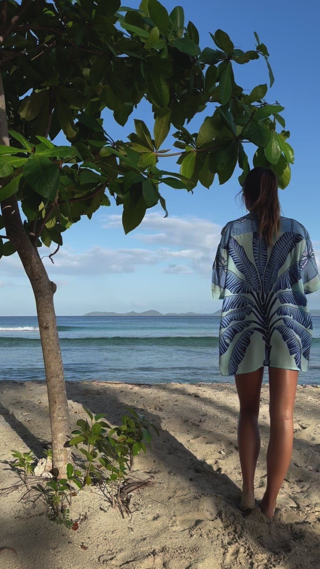 Lottie walks into the sea in unisex Banana Tree Blue silk festival shirt – luxury beachwear by Pink House Mustique on Mustique Island