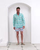 Model wearing men’s linen shirt in Agave Turquoise with matching turquoise and pink swim trunks by Lotty B Mustique