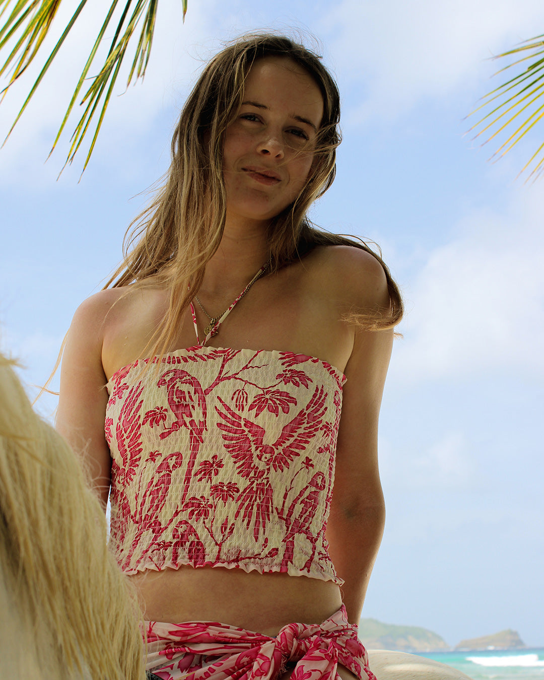 Model in silk crepe ruffle bandeau top in Parrot Pink at Lagoon Bay Mustique – strapless beachwear with island style