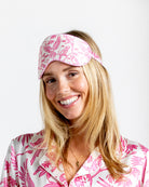 Woman wearing luxury silk eye mask in pink parrot print with matching silk pajamas by Lotty B Mustique
