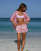 Coordinated pink Parrot print silk shorts and shirt set, model standing on sandy tropical shore