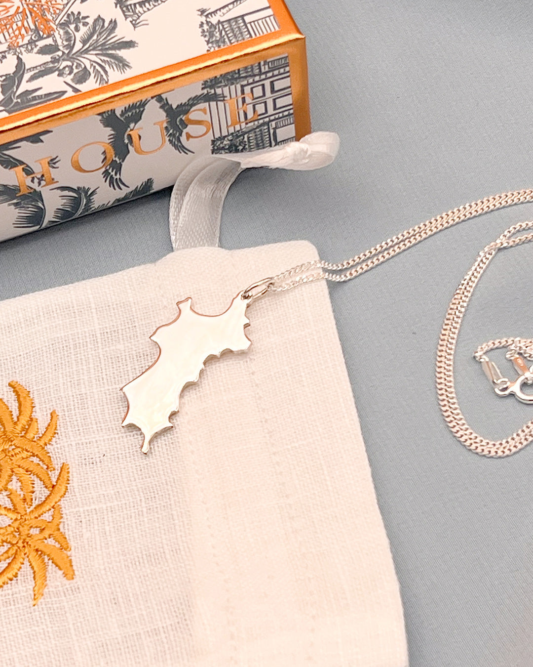 Close up hallmarked sterling silver Mustique island pendant necklace with Pink House Mustique packaging