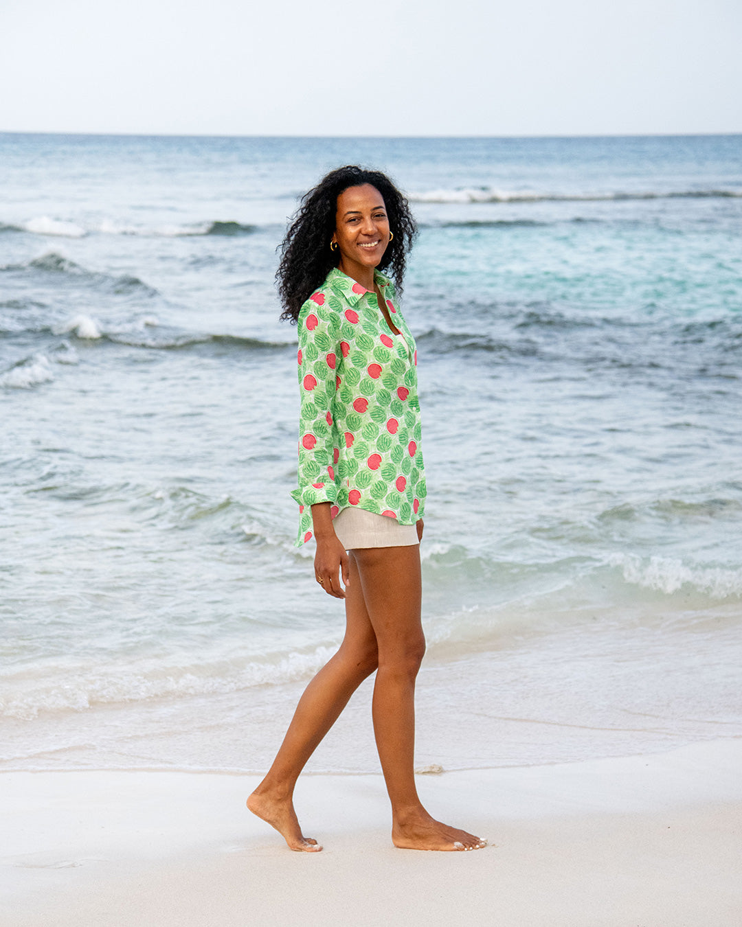Woman wearing Watermelon Green Anastasia linen beach shirt and natural shorts by the Caribbean sea