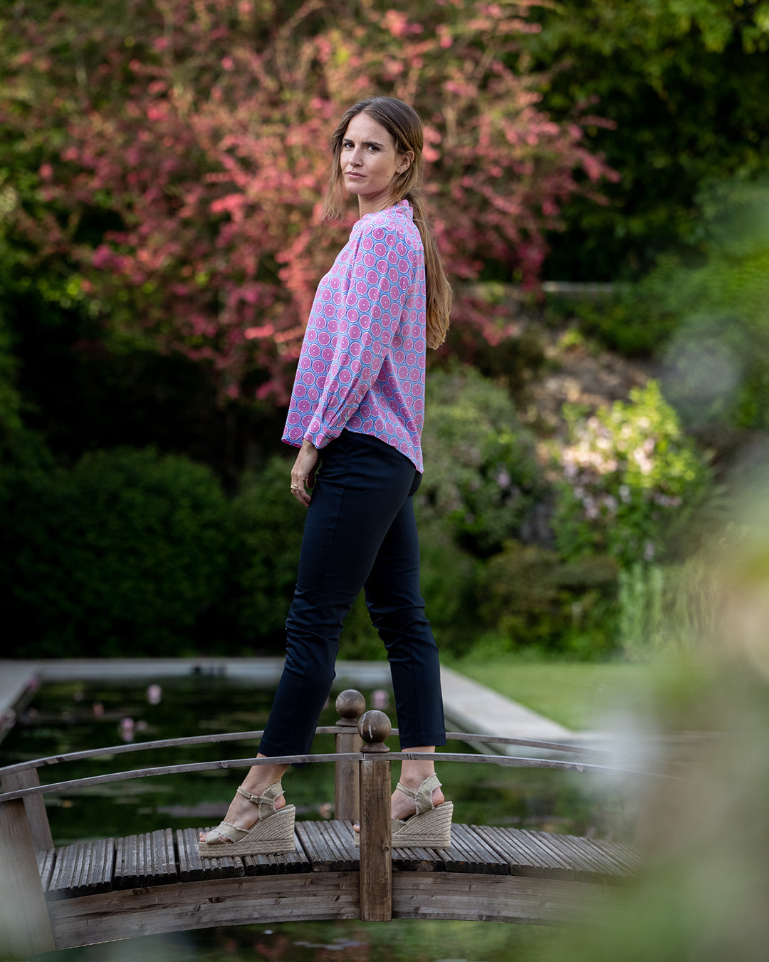 Woman standing on a wooden bridge in a garden setting